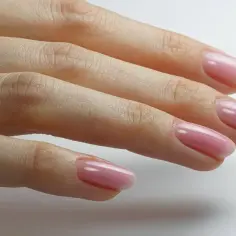 Dłoń z delikatnym, różowym manicurem w stylu clean girl. Paznokcie są zadbane, o naturalnym kształcie, z subtelnym połyskiem.